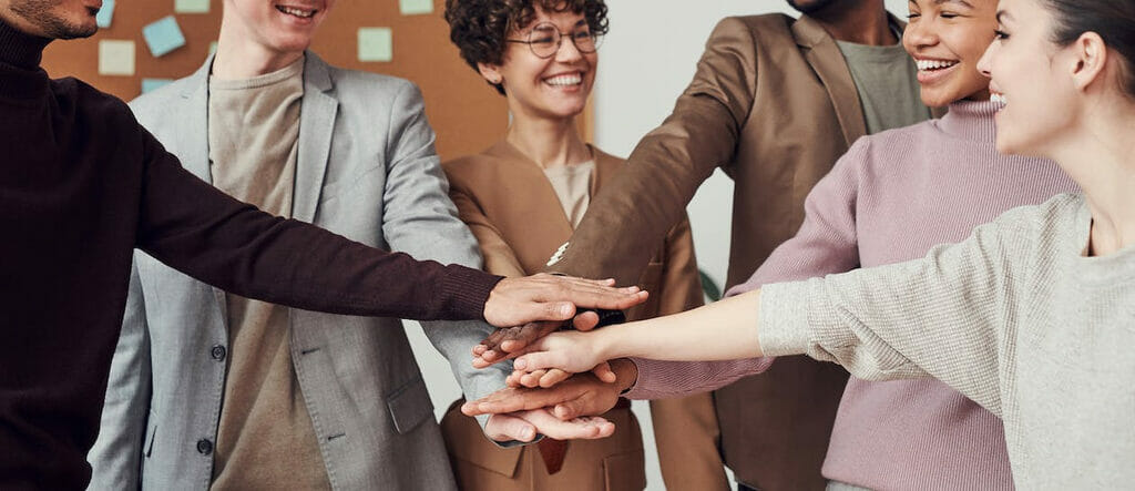 Smiling teachers putting their hands in the center of a group.