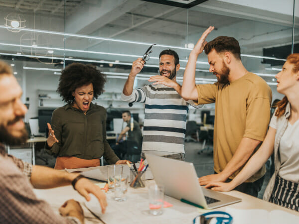 Five people  standing around a table frustrated over their group projects.